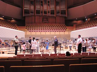 ミューザのステージに川崎市立登戸小学校の子たちとスダーンさんが集まっている写真。