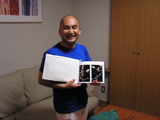 青い半そでの服を着た広上マエストロの写真。写真が載った本を両手に持っている。笑顔。