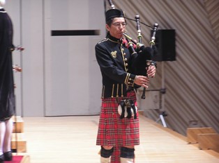 ステージで本場の衣装を身にまといバグパイプを吹いている十亀さん。