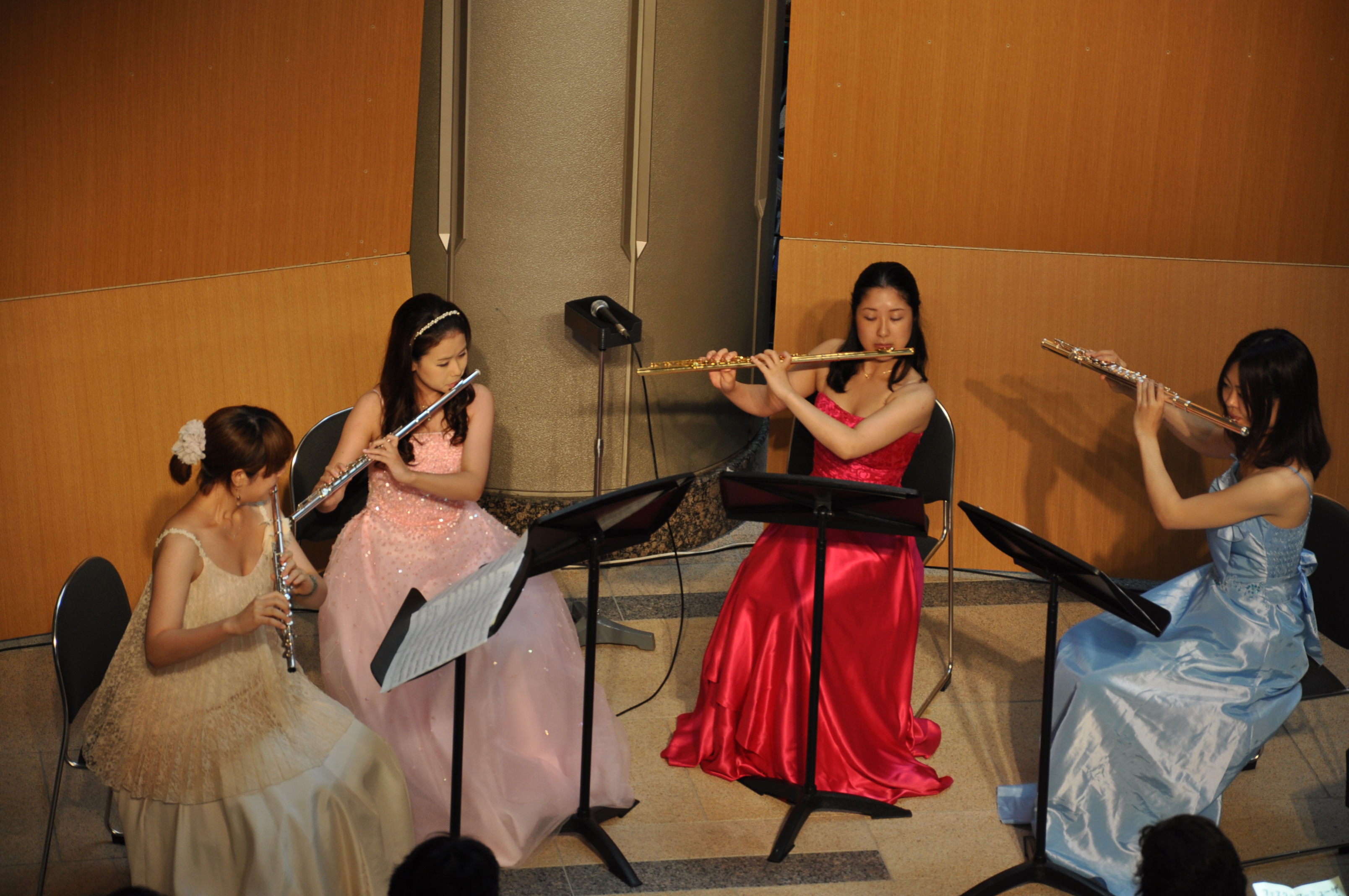 左から黄色、ピンク、赤、水色のドレスに身を包んだフルート奏者たちが演奏している様子。上からのアングル。