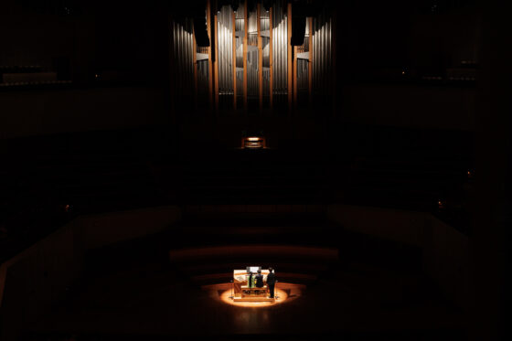 ホールで照明に照らされたパイプオルガン。パイプと、ステージ上で龍田さんと丁さんが演奏する移動演奏台のみにスポットライトが当たっている。