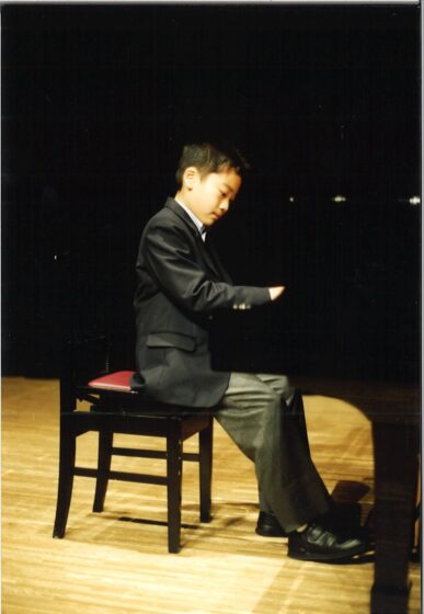 ピアノの発表会でピアノに向かう熊倉さんを右から撮影。写真の真ん中で右手を鍵盤にのせ、手を見つめている。