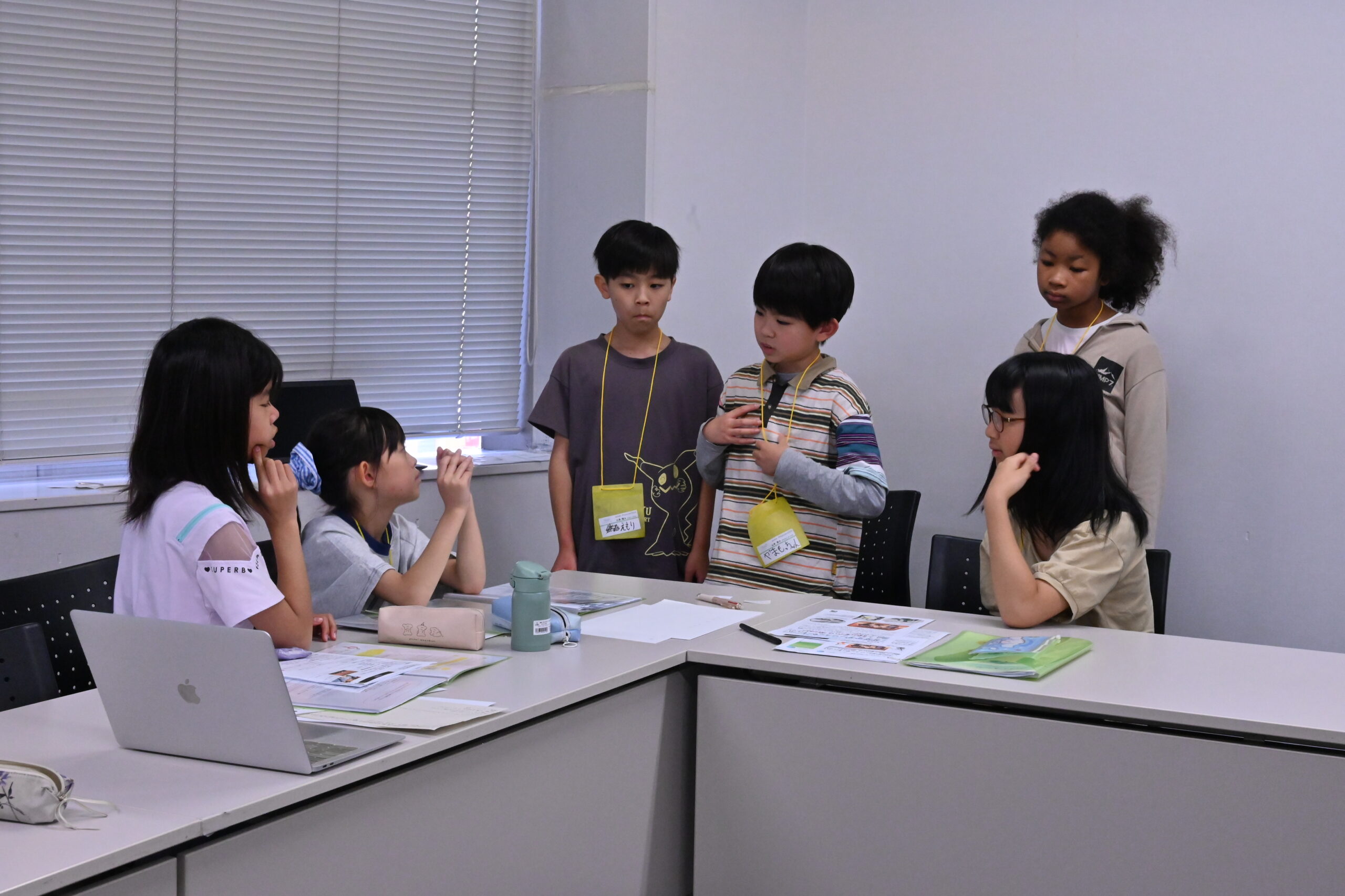 決まったことを広報班に伝える運営班の様子の写真。着席している広報班3名の近くに3人並んで立っている運営班メンバー。