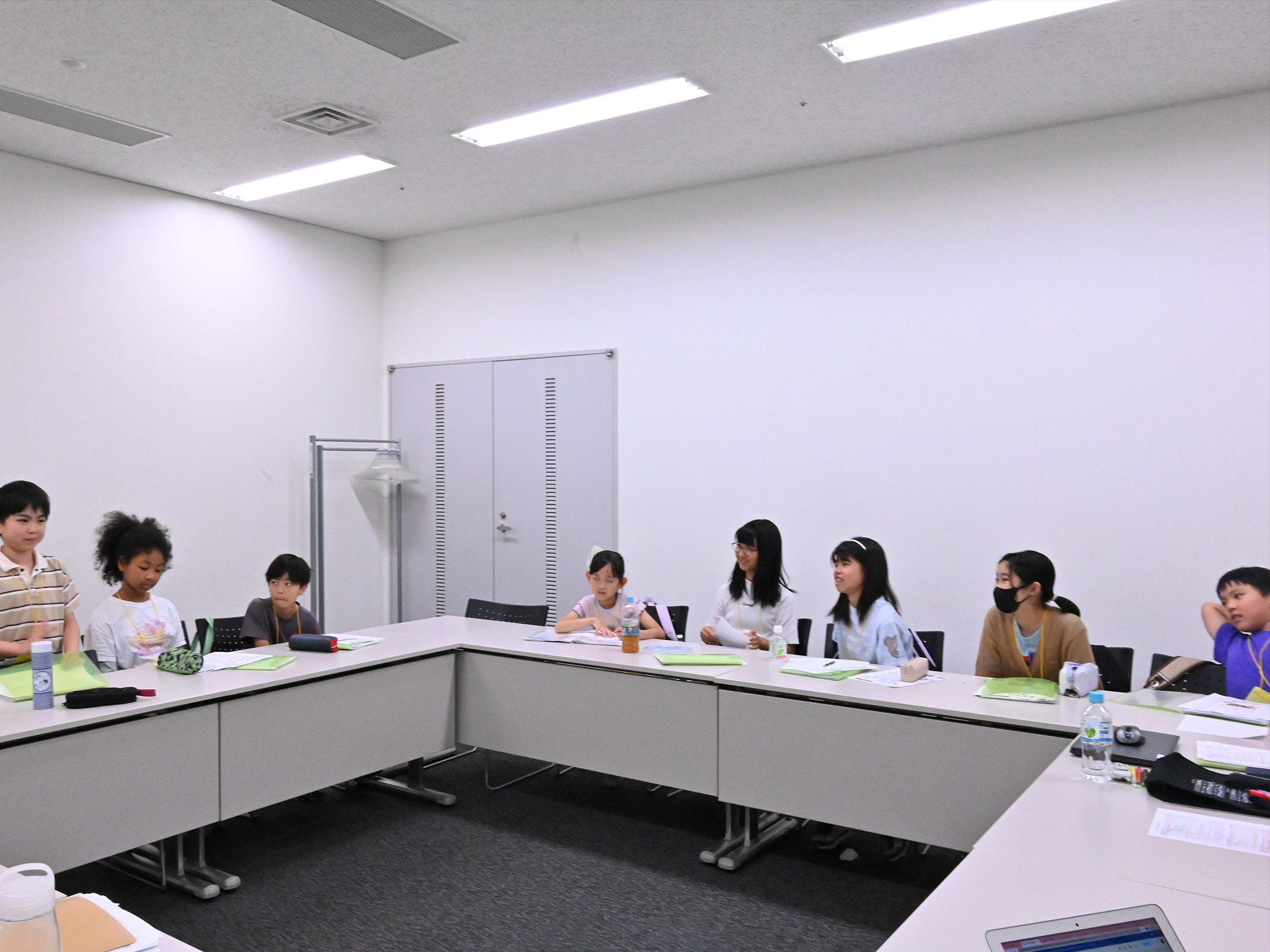 最初の会議室で、1人のメンバーが立って話しているのを他のメンバーが注目している写真。着席しているメンバーは笑顔で聞いている。