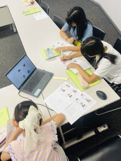 机上に並んだプログラムやパソコンと、各々作業をしている広報班メンバーが上から撮られた写真。