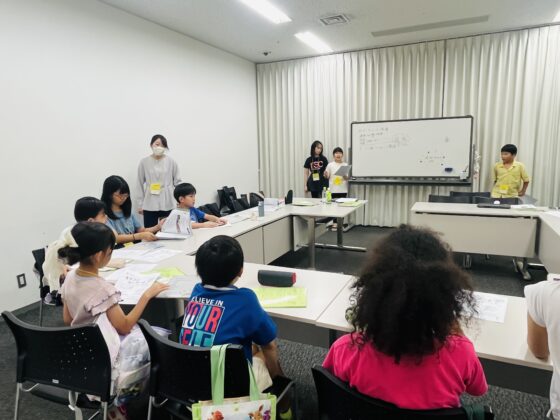 ホワイトボードの前に企画班3人が立ち、他のメンバーに向かって話している写真。