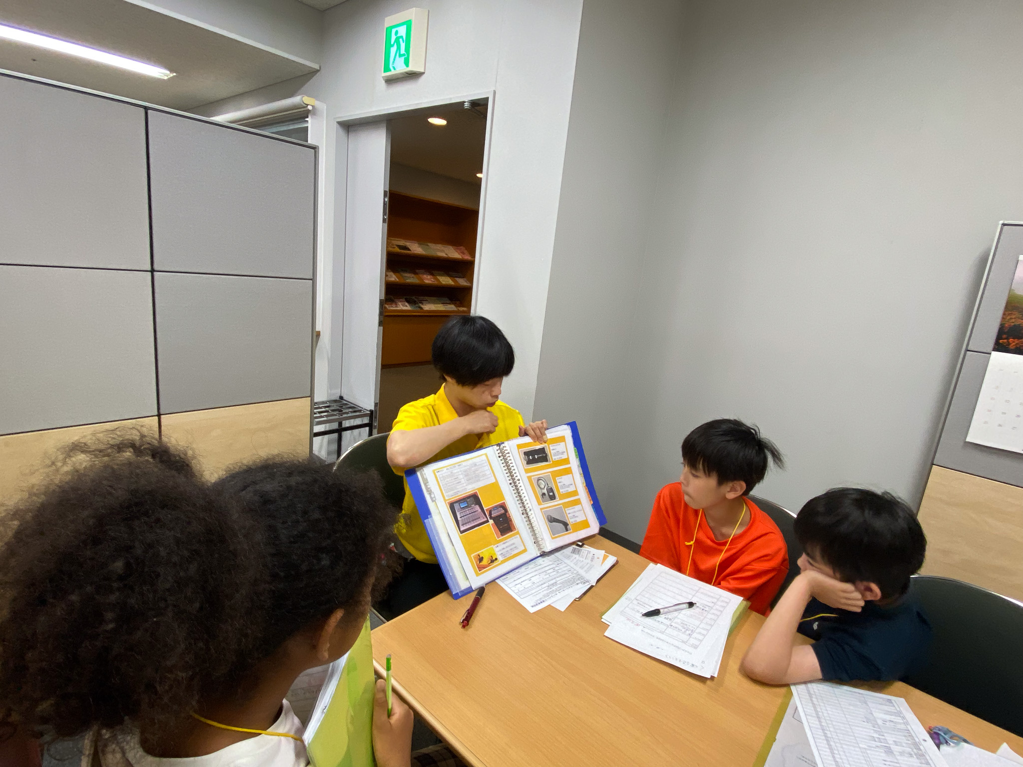 受付スタッフがファイルを開き、運営班メンバーに見せている写真。運営班3人はファイルをよく見ている。