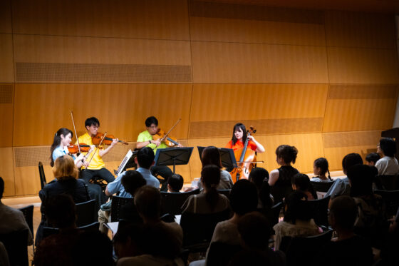 満席のお客様が演奏者のすぐ近くから座っている会場で演奏する東京交響楽団弦楽四重奏メンバーの写真。演奏者はそれぞれ水色、黄色、黄緑、オレンジのポロシャツを着用してカラフルな舞台