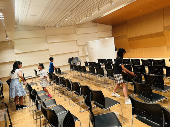 会場の市民交流室内でお客様のための椅子100脚程を並べているジュニア・プロデューサーたちの写真