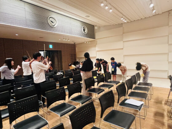 客席の間にいる4名の出演者に向かって、1列に並びお辞儀をしているジュニア・プロデューサーたちの写真