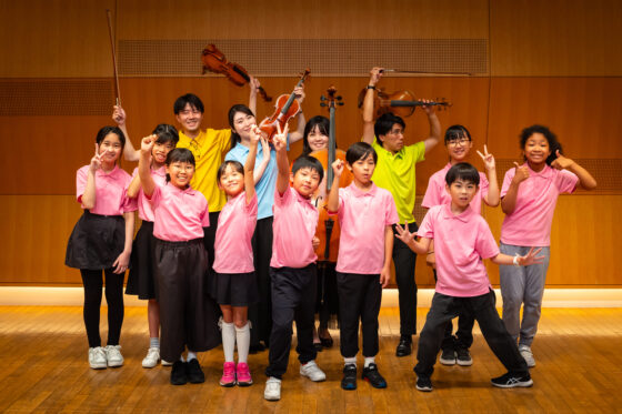 出演者とジュニア・プロデューサーの集合写真。出演者たちは後列で楽器を掲げ、ジュニア・プロデューサーたちは前列でガッツポーズやピースをしてみんな達成感のある笑顔