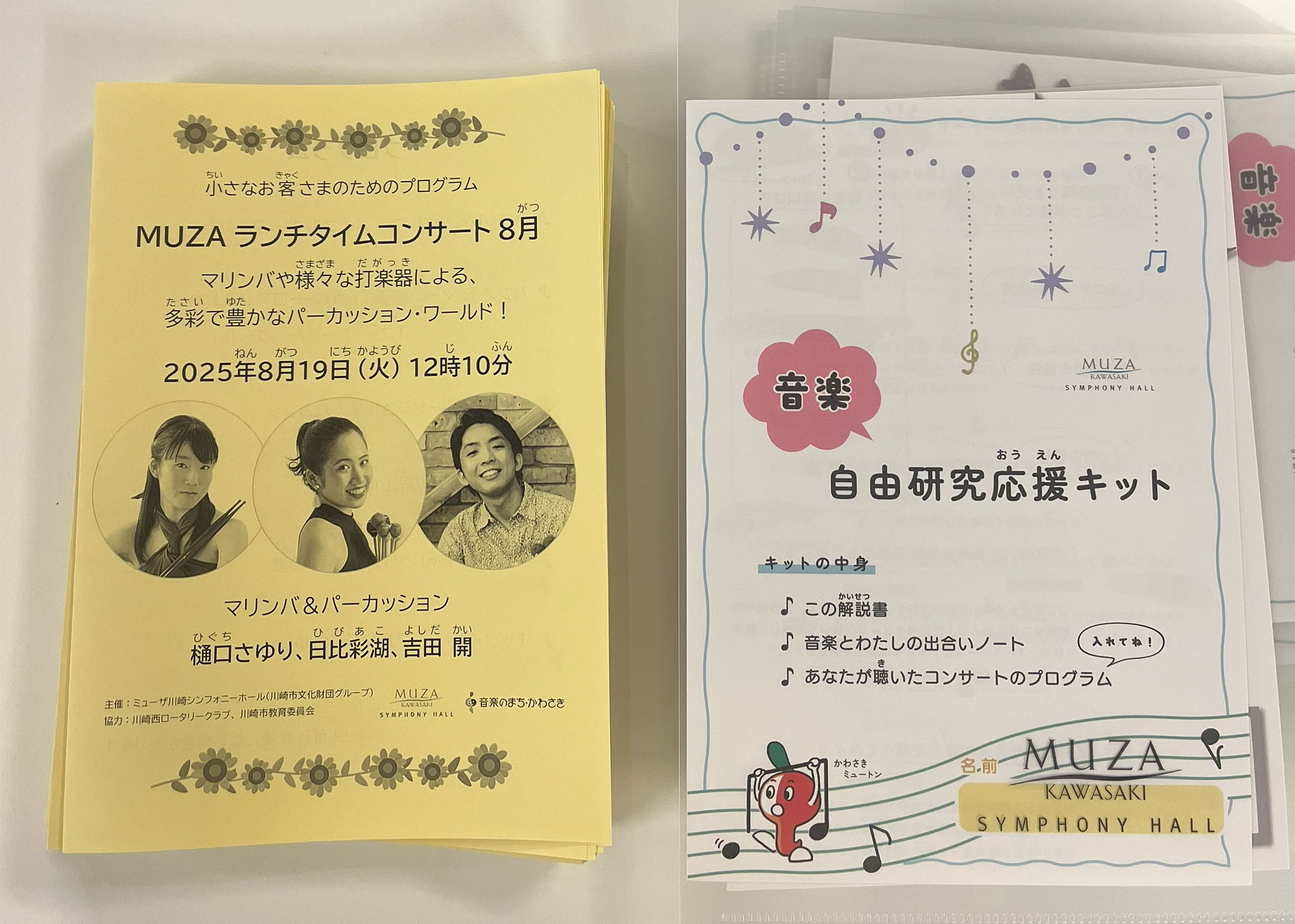 机に置かれた『小さなお客さまのためのプログラム』と『自由研究応援キット』の写真。『小さなお客さまのためのプログラム』は黄色の紙に公演タイトルや出演者の写真、ひまわりのイラストが書かれており、『自由研究応援キット』はファイルの中に白色の冊子があり、中身が「この解説書」「音楽とわたしの出合いノート」「あなたが聴いたコンサートのプログラム（入れてね）」と書かれている。