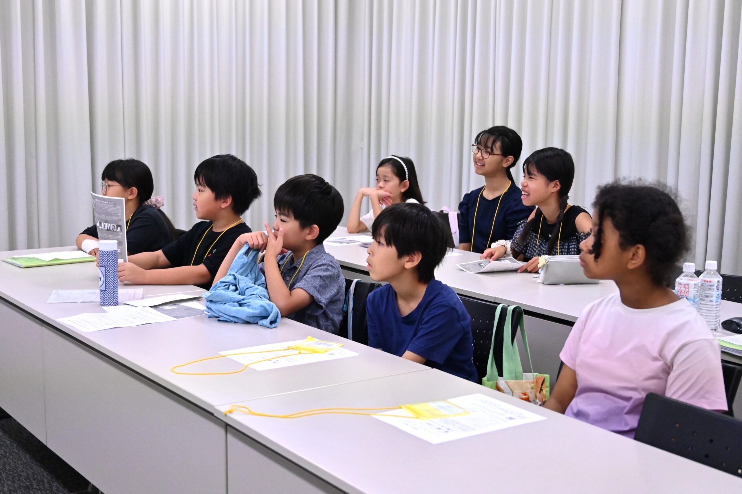 2列に並んだ長机に座って前方を笑顔で見ている8人のジュニア・プロデューサーたち。