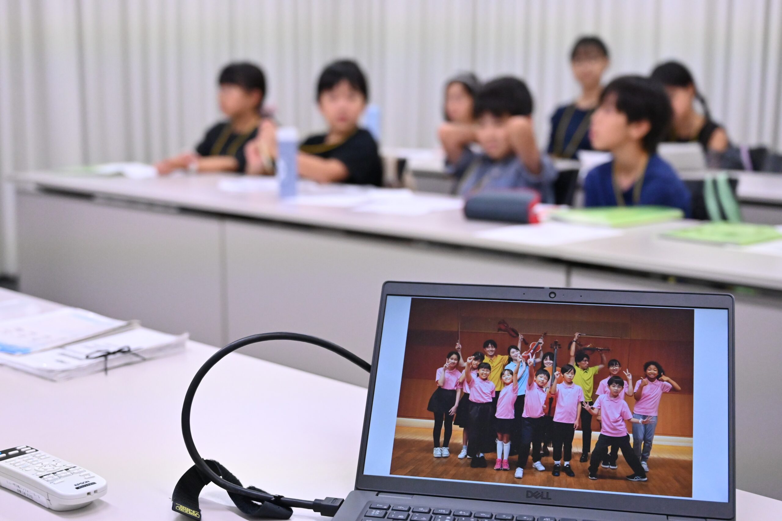 終演後に出演者と撮った写真が映し出されたパソコンにピントが当てられ、そのパソコンの奥にぼやけて写る話し合い中のジュニア・プロデューサーたち。
