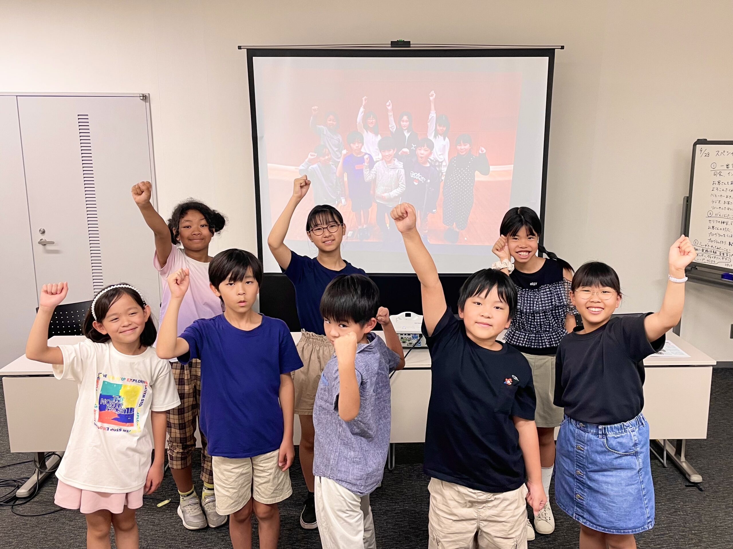 バックのスクリーンに初回活動日に撮影したガッツポーズの集合写真を映し、その前に同じ順番でほとんど同じポーズをして写るジュニア・プロデューサーたち。