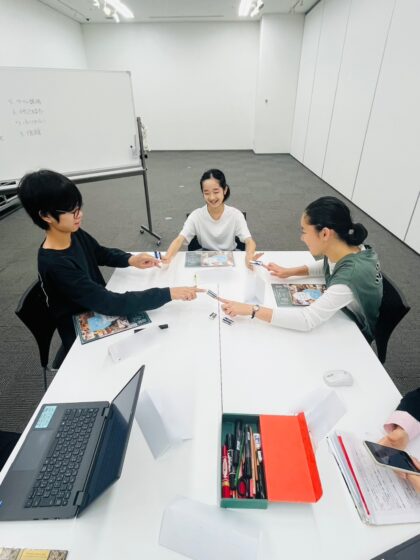 座ったまま、両手を相手の方に伸ばし、お互いの人差し指だけで消しゴムを挟み、見事にバランスを取っている写真。