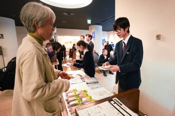 ホールロビーの主催受付の隣でお客様に景品の入浴剤を渡すリトルミューザメンバーの写真