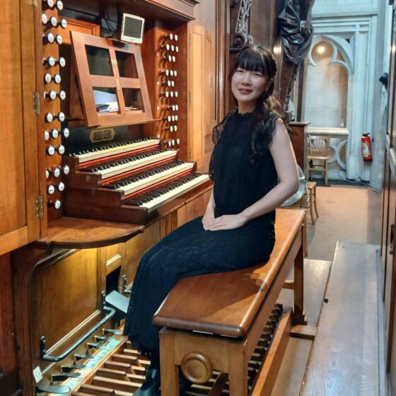 パイプオルガンのベンチに座り、こちらを向く澤菜摘。写真左側にパイプオルガン。