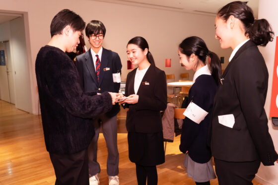 舞台裏でリトルミューザの1人が指揮者の川瀬賢太郎さんに入浴剤を手渡している写真。メンバーはよく笑っている。