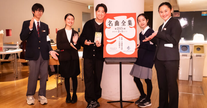 川瀬さんとリトルミューザ4人が「名曲全集」の大入り袋の掲示物を囲んで笑顔で並んでいる集合写真