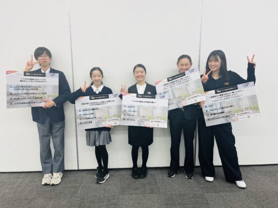 掲示していたクイズの問題のプレートを1人ずつ持って、横一列に並ぶメンバー4人と、右端に大学生アドバイザーの写真。みんな笑顔でピースして立っている。