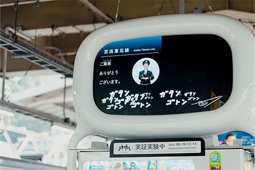 駅のホームの自動販売機上に設置されたエキマトペの写真。エキマトペのディスプレイには、電車が離れていく様子のイラストと「ガタンゴトン」の手書き文字。アナウンスの手話映像と字幕が表示されている。